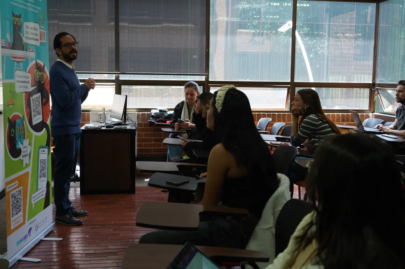 Un formador habla frente a estudiantes universitarios junto a un pendón de Colombiacheck